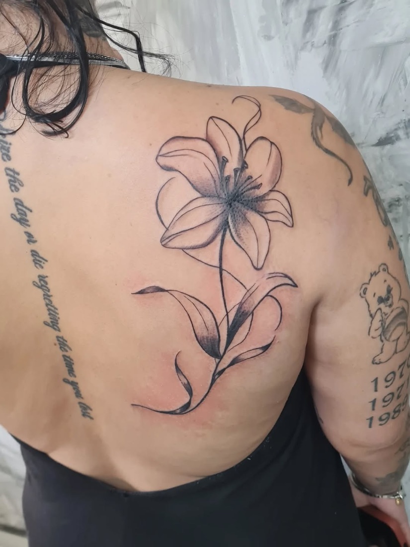 Tatuagem fine line de lírios nas costas, com frase ao lado da coluna
